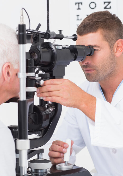 Male,Optometrist,Examining,Senior,Mans,Eyes,Through,Slit,Lamp,In Eye Exam